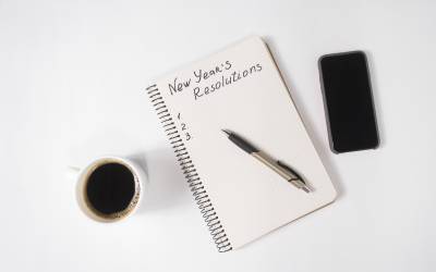 Next to a coffee cup and smart phone, a notebook reads: New Year's Resolutions