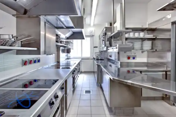 A clean commercial kitchen featuring stainless steel prep stations, cooking appliances, and tiled floor drainage.